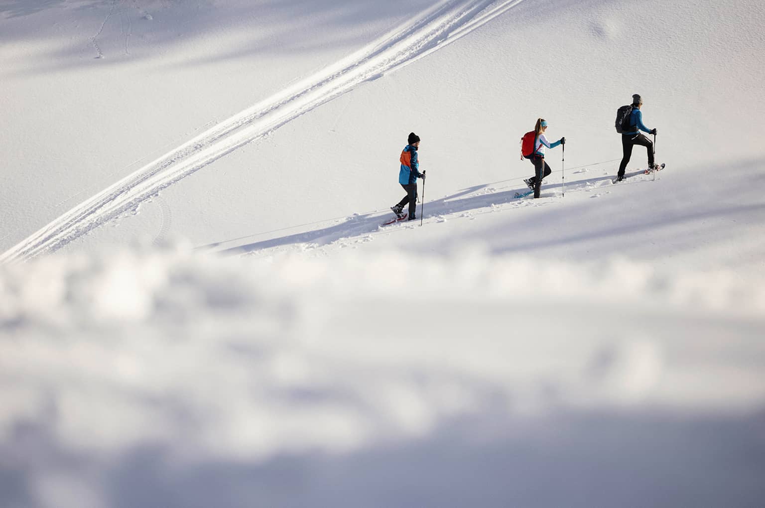 Drei Schneeschuhwanderer im Tiefschnee bei Sonnenschein